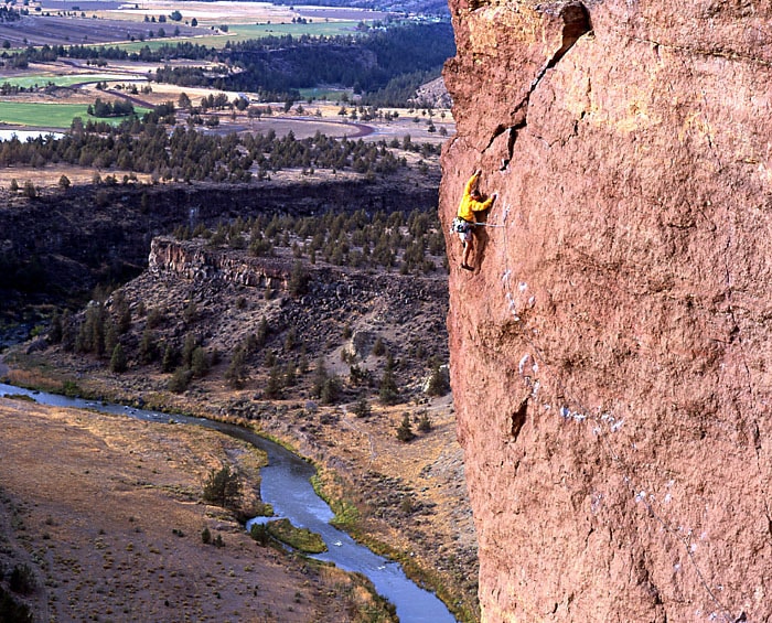 Climb instructor in orange jacket rock climbing at great height with view of smith rock below